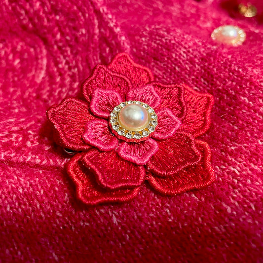 Broderad brosch med röda och rosa tråda. En personlig detalj som gör en köpt kofta mer personlig. Knappen i mitten är en extraknapp som följde med koftan vid köpet.