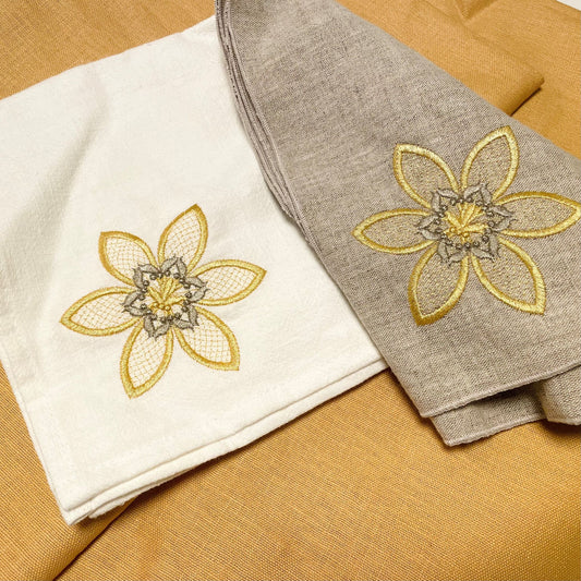 Tygservetter av halvlinne och linne med broderade blommor med guldfärgad tråd och lite beige. Vit linneservett och oblekt naturfärgad halvlinneservett.
