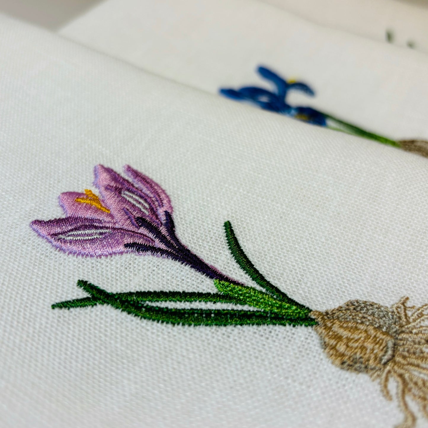 Närbild på broderad linneservett. Tygservett av vitt linne med broderad krokus. Krokusen har löken med.