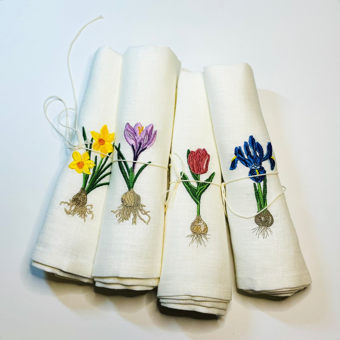 Linneservetter med fyra olika vårblommor vårlökar broderade. Blå iris, gul påsklilja, rosa tulpan och lila krokus. Alla blommor har sina lökar med. Ett set tygservetter med vårtema