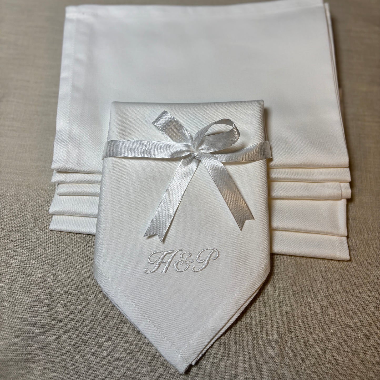 Klassiska lyxiga vita tygservetter av tät och fin bomull. Monogram broderat med vit brodyrtråd. H&P i kursiv stil i nedre hörnet. Ett vitt satinband är knutet löst runt servetten med en rosett.