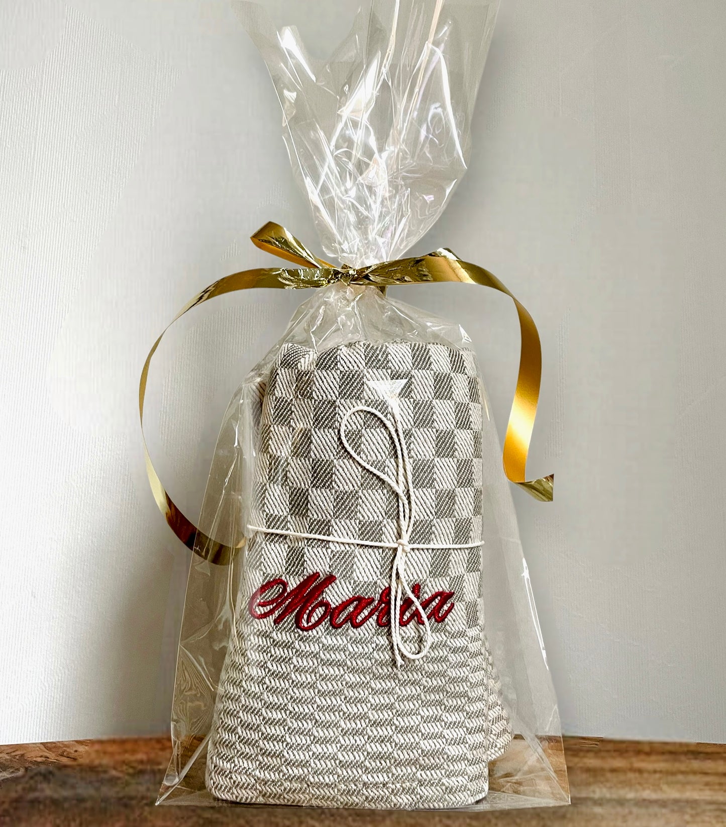 Linnefärgad rustik bakduk med vävt rutmönster och broderat namn i mörkrött. Servetten eller handduken är packad i cellofanpåse och har guldfärgat presentsnöre runt. Färdig present att ge bort.