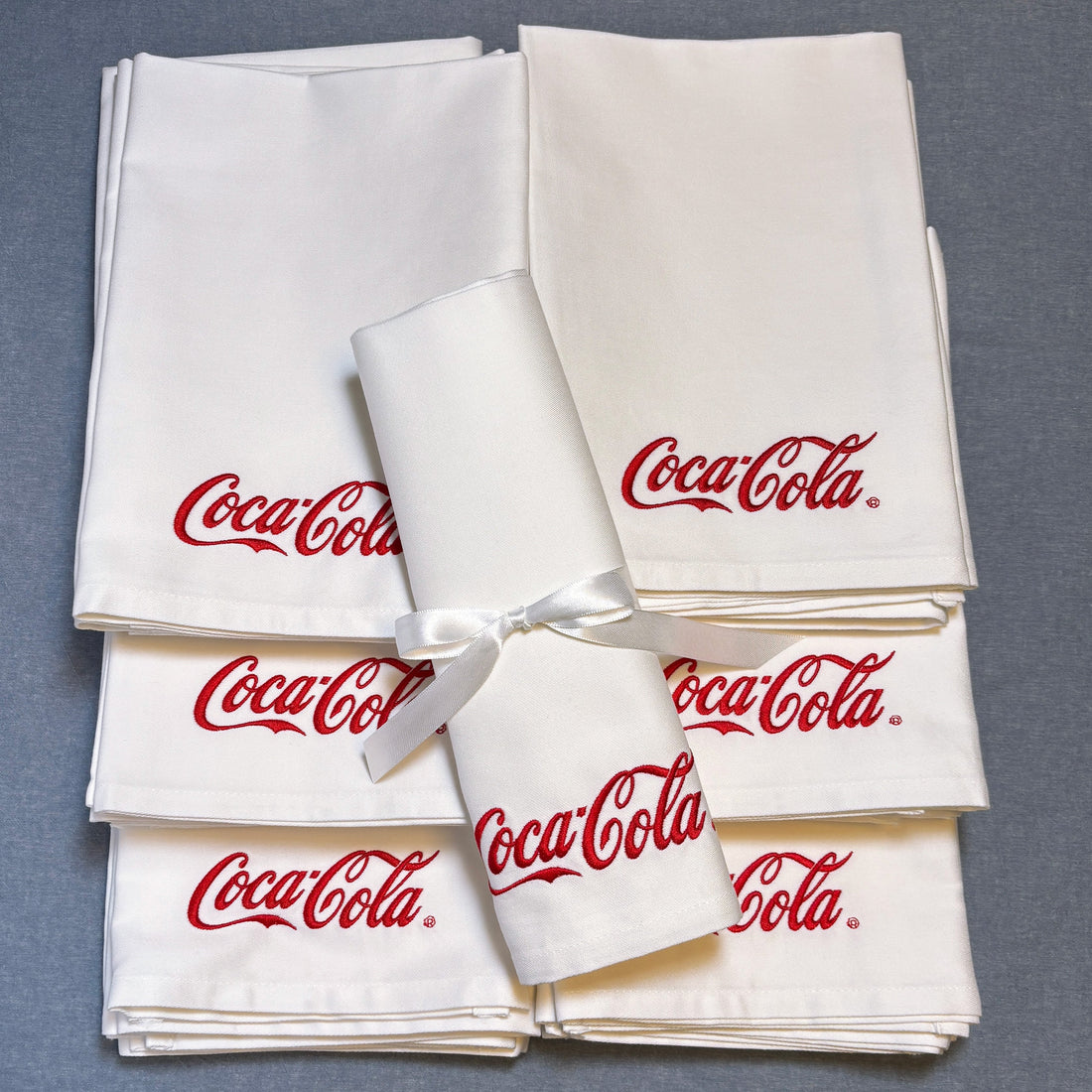 Vita tygservetter med röd brodyr Coca-Cola. Ligger på en blå duk.