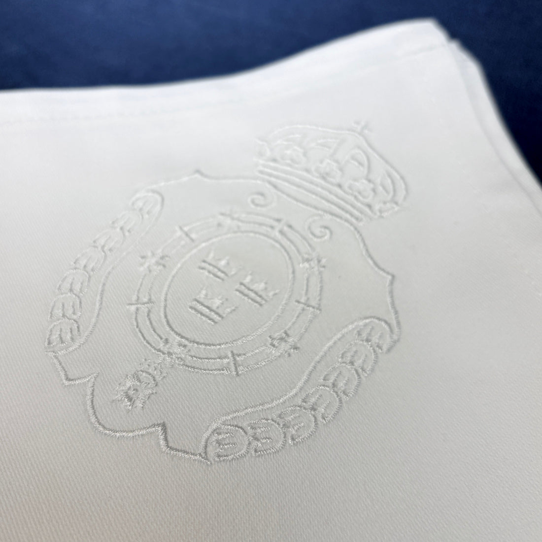 Broderade vita tygservetter av bomull. Närbild på brodyren som är Svea Livgardes emblem. Vit brodyr på vit tygservett.