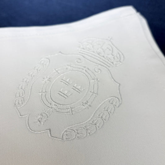 Broderade vita tygservetter av bomull. Närbild på brodyren som är Svea Livgardes emblem. Vit brodyr på vit tygservett.
