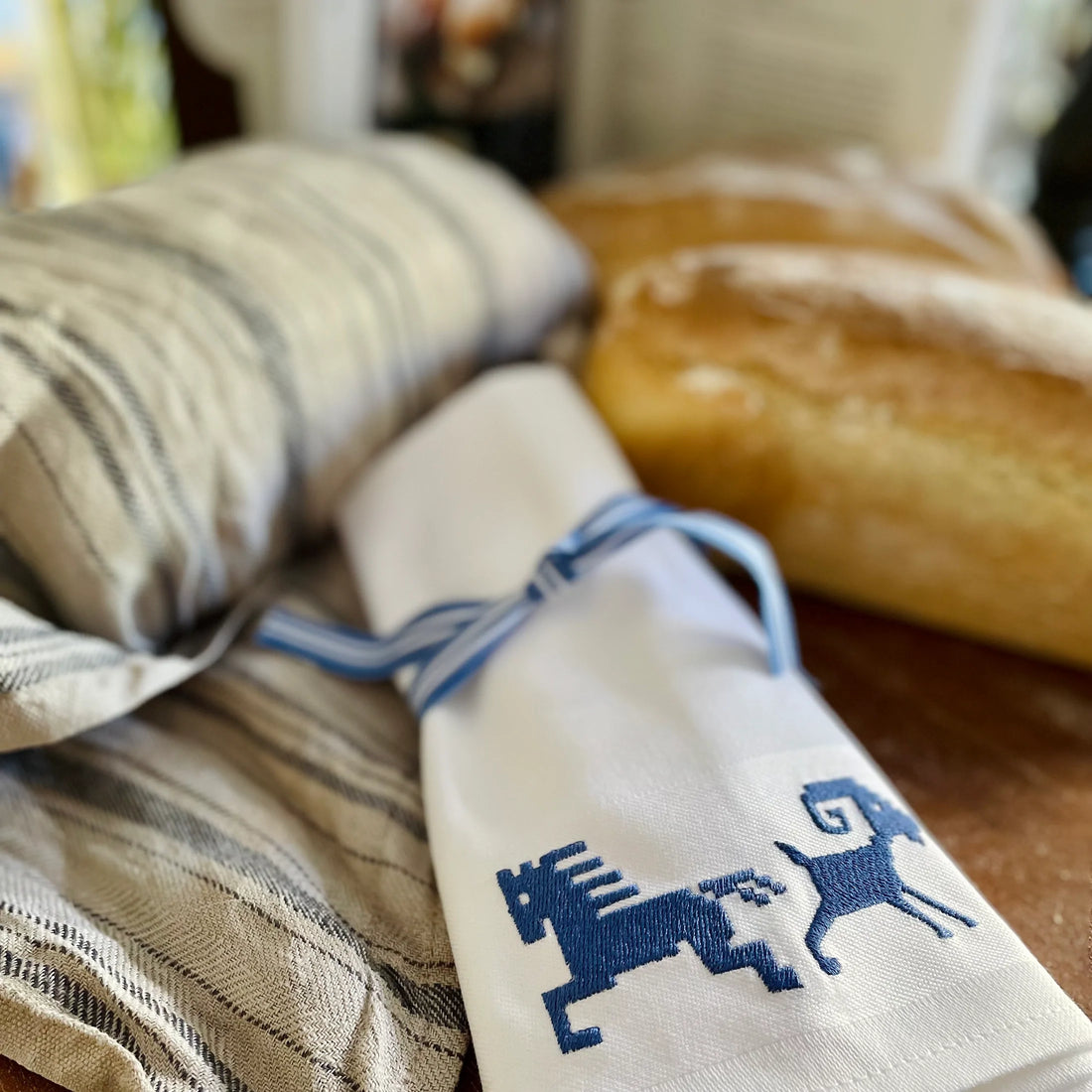 Vita tygservetter vid med broderade nordiska motiv i blått. På skärbräda med nybakat bröd.