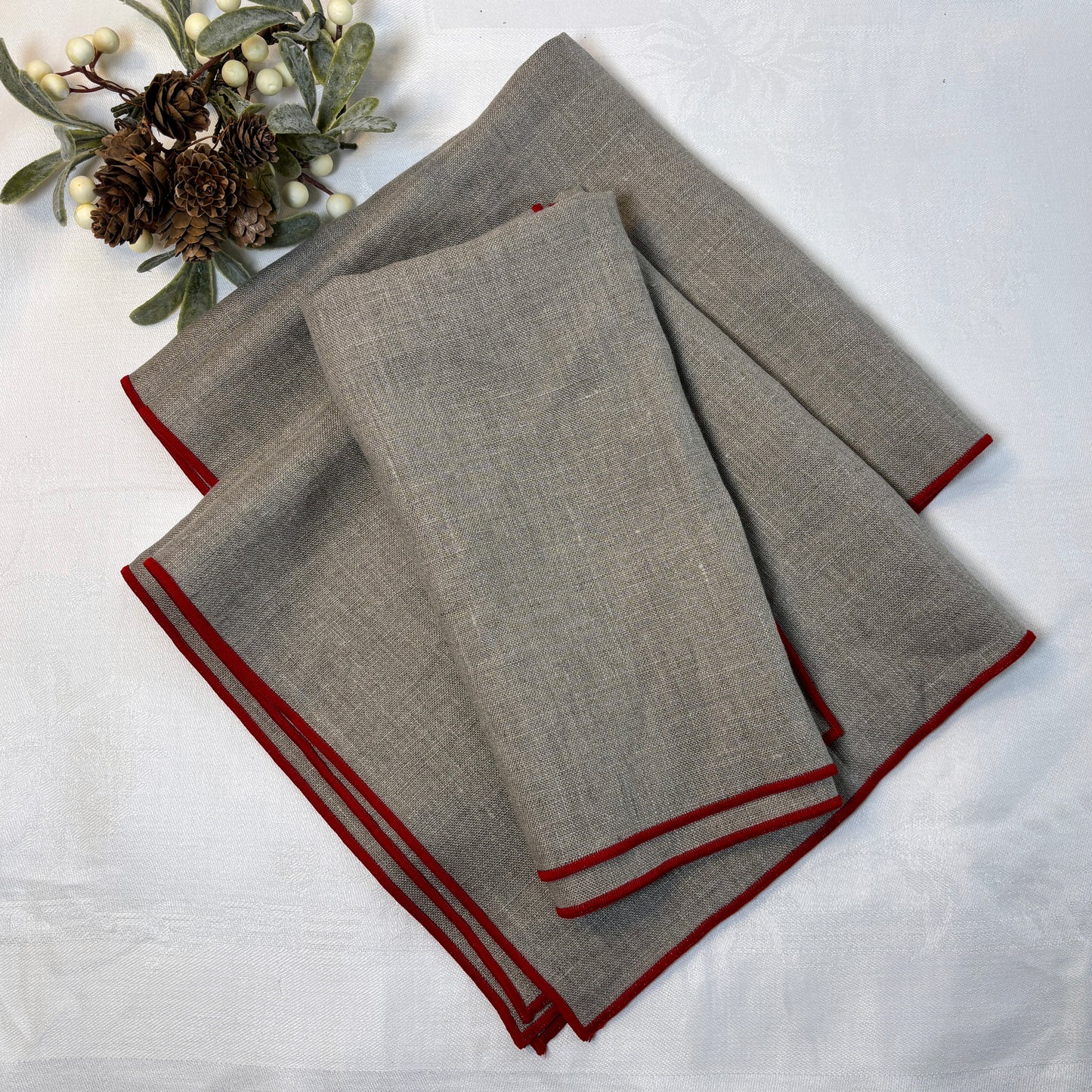Naturfärgade linneservetter med röda smala kanter. Ligger vikta på en vit linneduk.