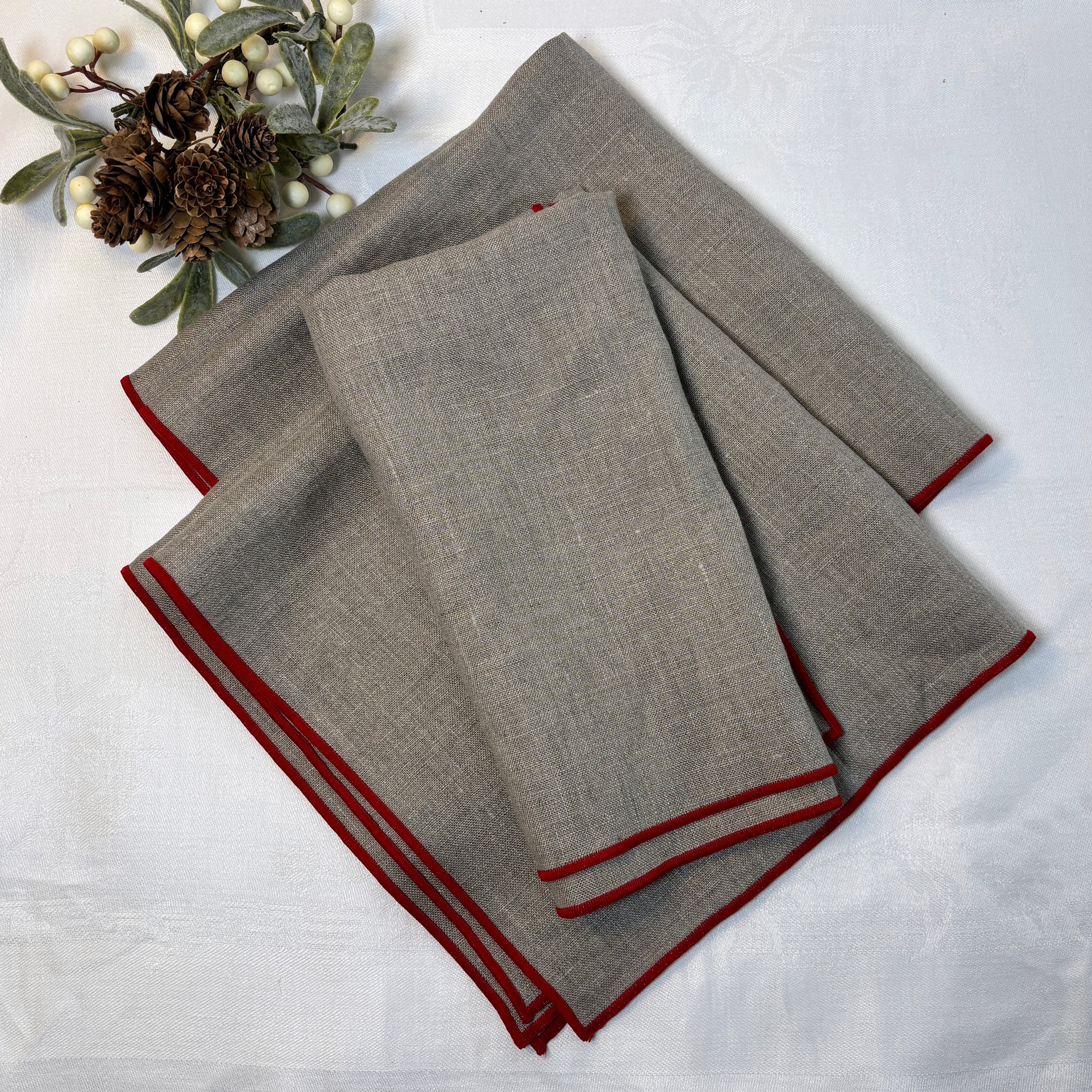 Naturfärgade linneservetter med röda smala kanter. Ligger vikta på en vit linneduk.
