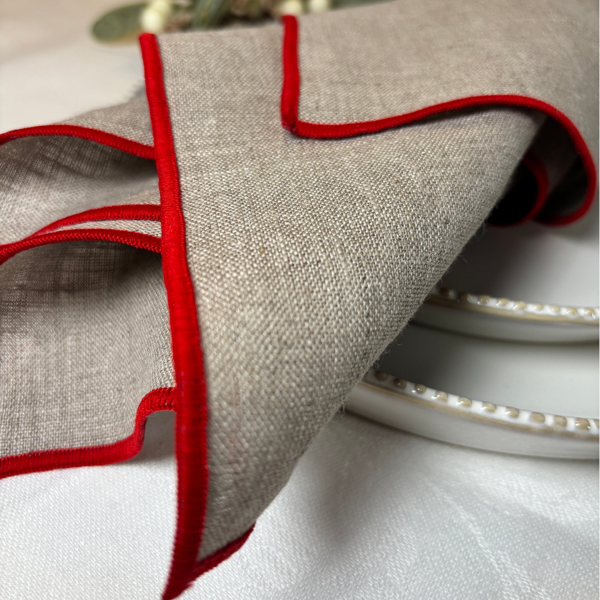 Närbild av naturfärgad linneservett som har röda sydda kanter.