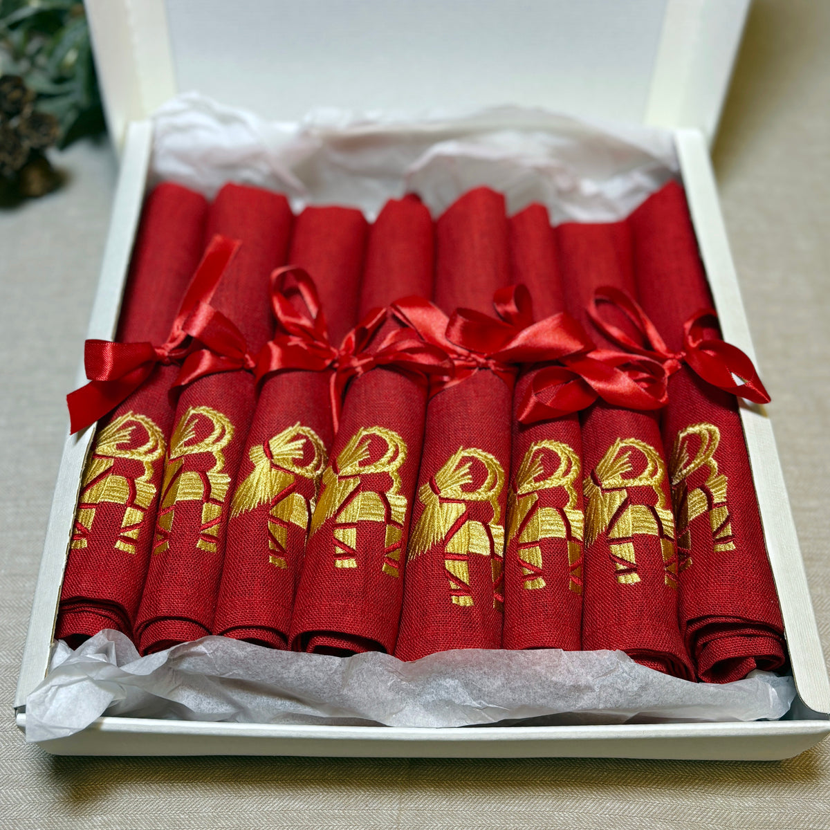 Röda linneservetter med broderade halmbockar i guldfärgad och röd tråd. Röd rosett kring varje servett. 8-pack i en krämvit presentkartong.