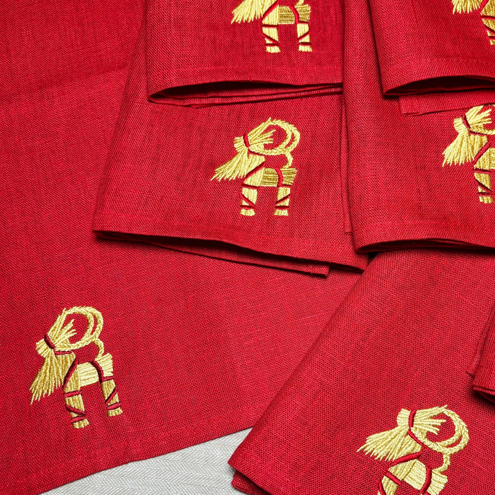 Röda linneservetter med broderade halmbockar i guldfärgad och röd tråd. 