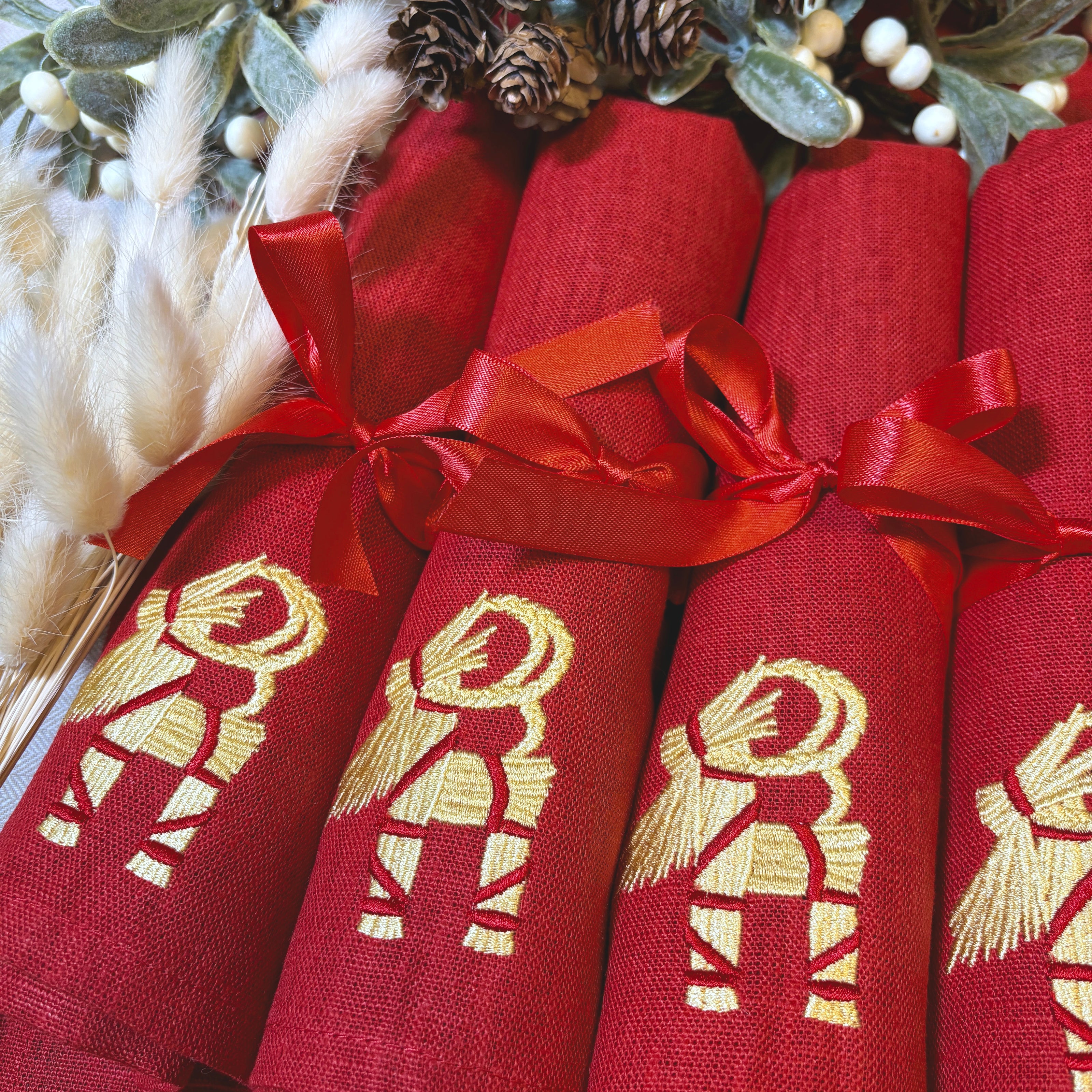 Röda linneservetter med broderade halmbockar i guldfärgad och röd tråd. Röd rosett kring varje servett.