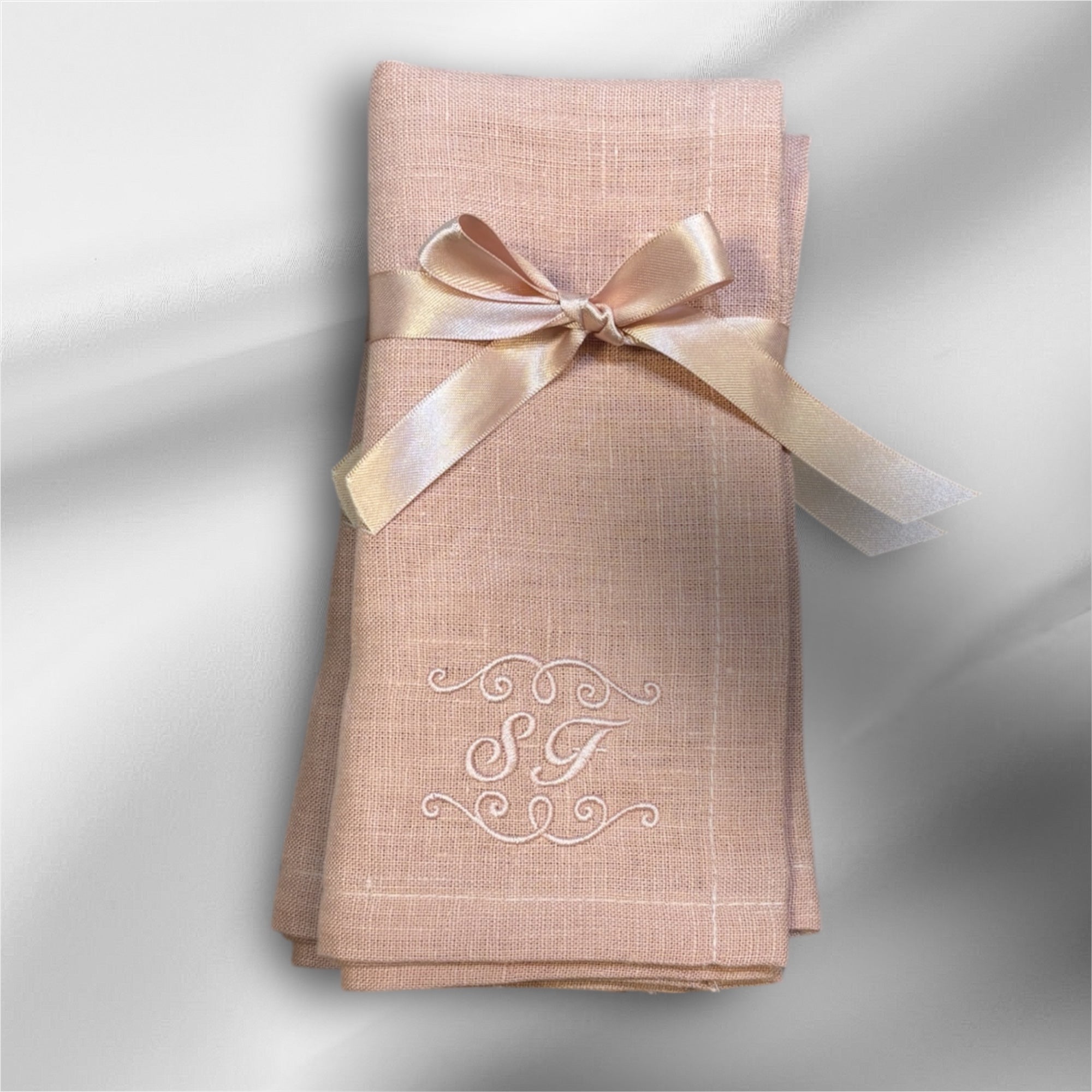 Rosa linneservett med rosa band knutet med rosett och rosa initialer samt dekor broderat. Vikt så den broderade kanten med initialerna SF visas upp.