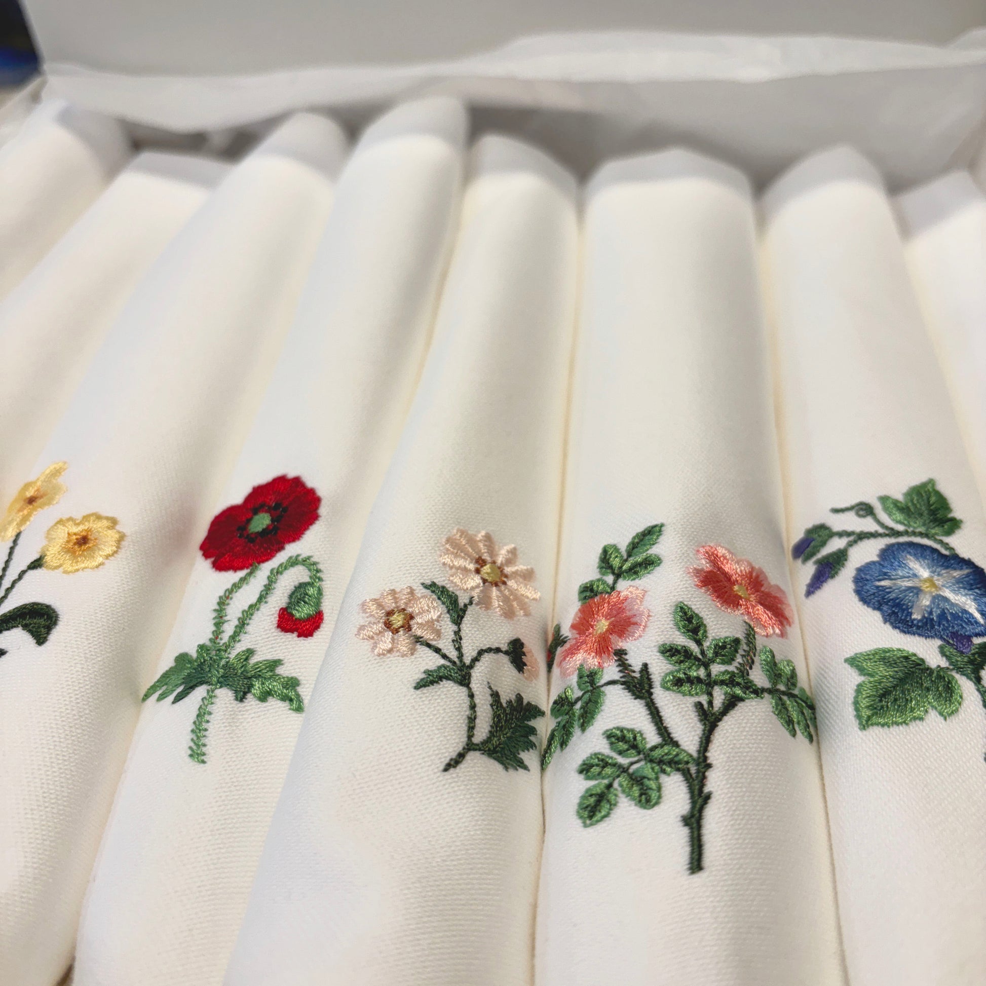 Vita tygservetter med olika blommor broderade på vardera. Ligger i en presentask. Primrose, pion, tusensköna, vildros, MorningGlory