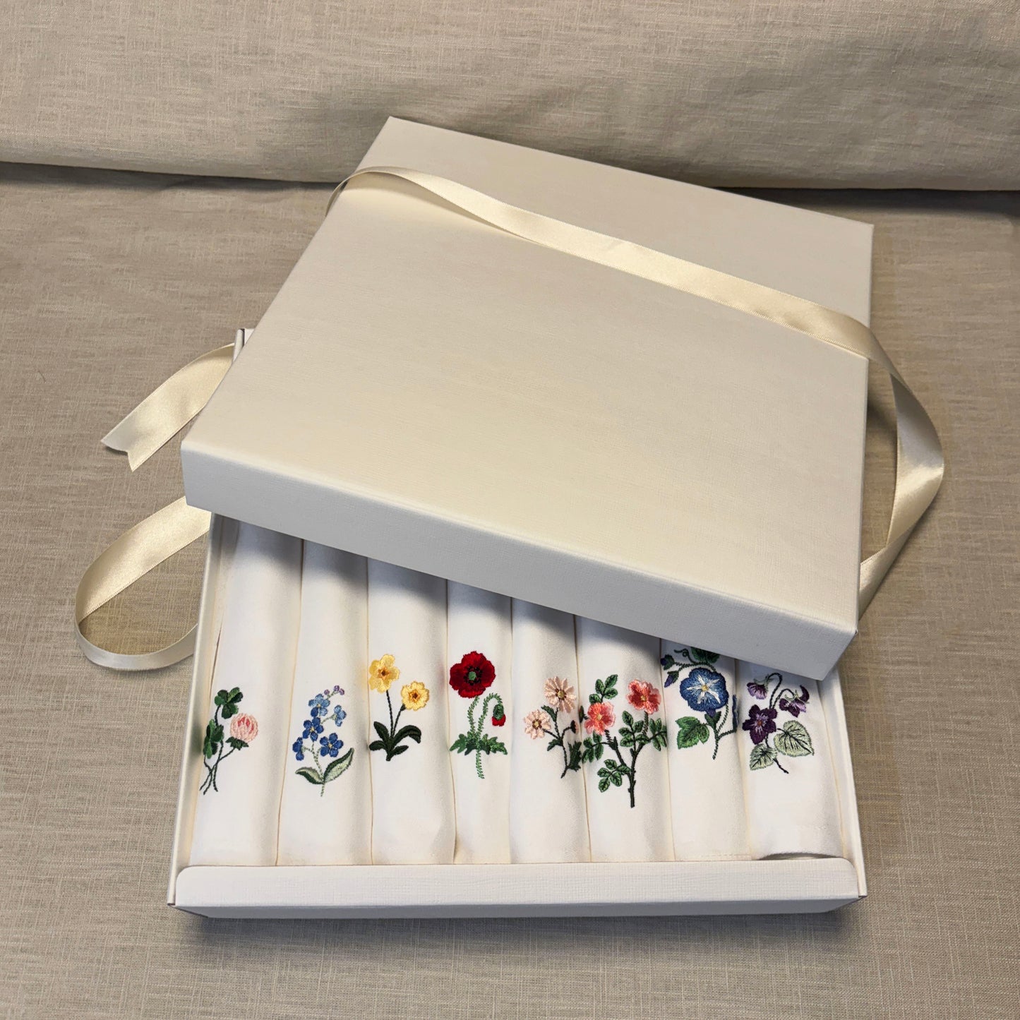 8 stycken vita tygservetter med olika blommor broderade på vardera. Ligger i en presentask. Klöver, forgetmenot, Primrose, pion, tusensköna, vildros, MorningGlory och Borage