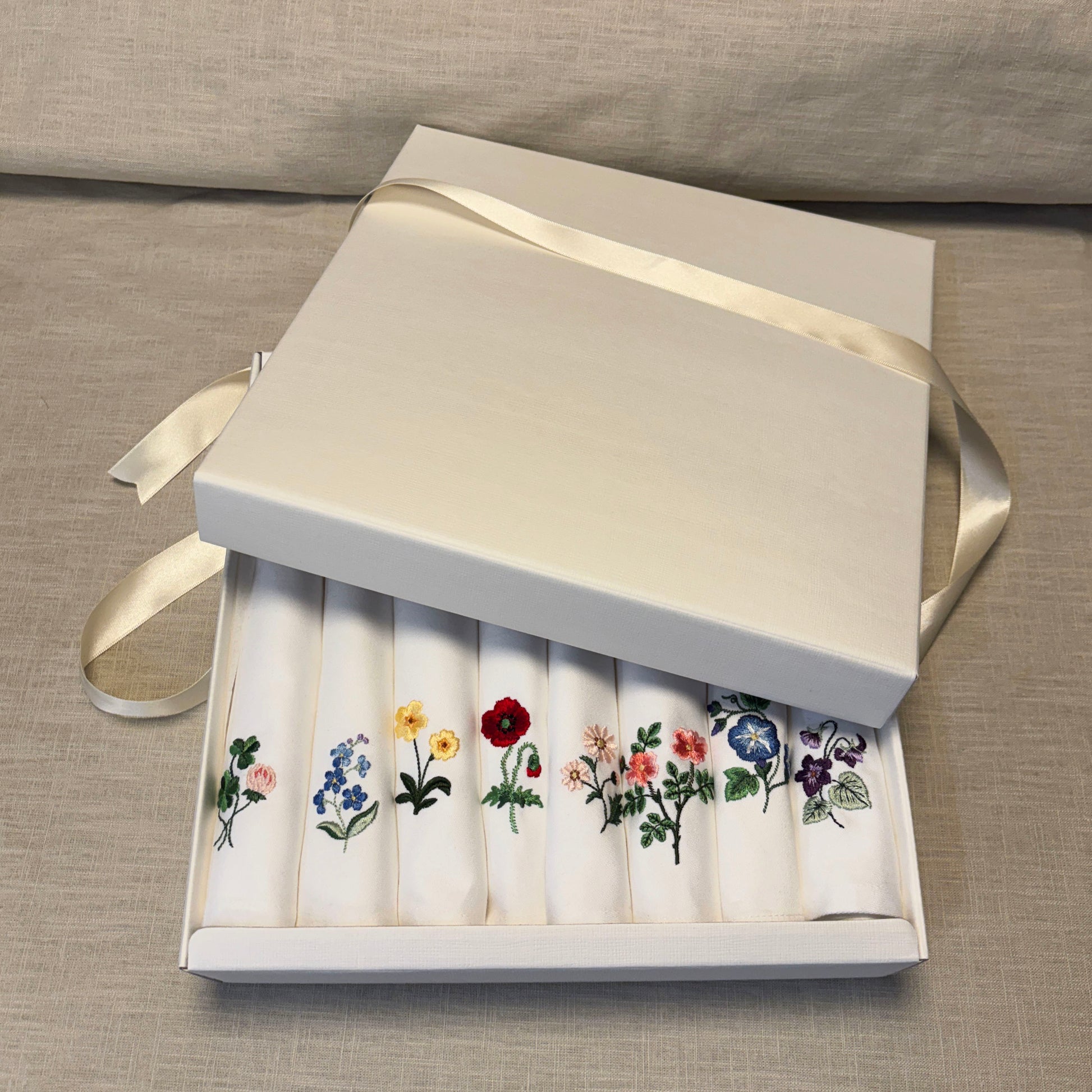 8 stycken vita tygservetter med olika blommor broderade på vardera. Ligger i en presentask. Klöver, forgetmenot, Primrose, pion, tusensköna, vildros, MorningGlory och Borage